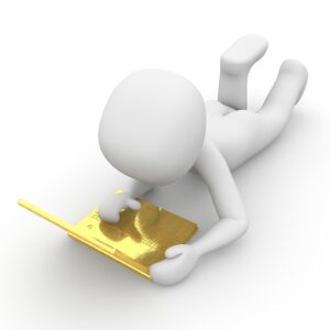 Kleine weiße Figur liegt auf dem Boden vor einem gelben aufgeklappten Laptop